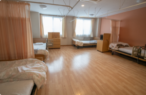 複数ベッドが配置された明るい多床居室。木製家具と温かみのある内装。