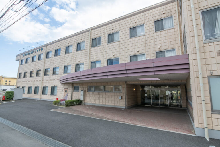 介護施設の玄関棟。紫色のひさし、自動ドア、車寄せを備えた現代的な建築
